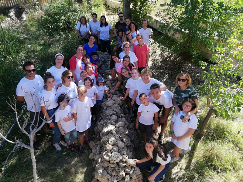 Foto de grupo de las familias de AXA de Todo Corazón que nos visitaron, con el muro de piedra seca que levantaron ya construido.