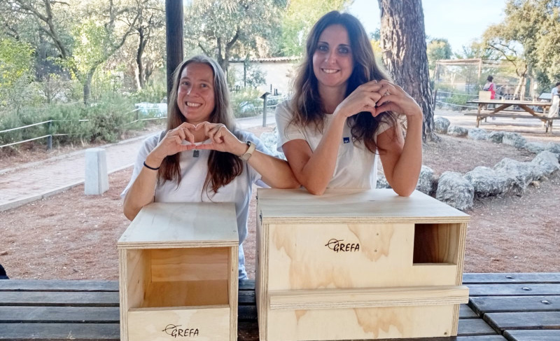 Dos trabajadoras de "AXA de todo corazón", junto a las cajas nido para cernícalo y lechuza que ayudaron a ensamblar.